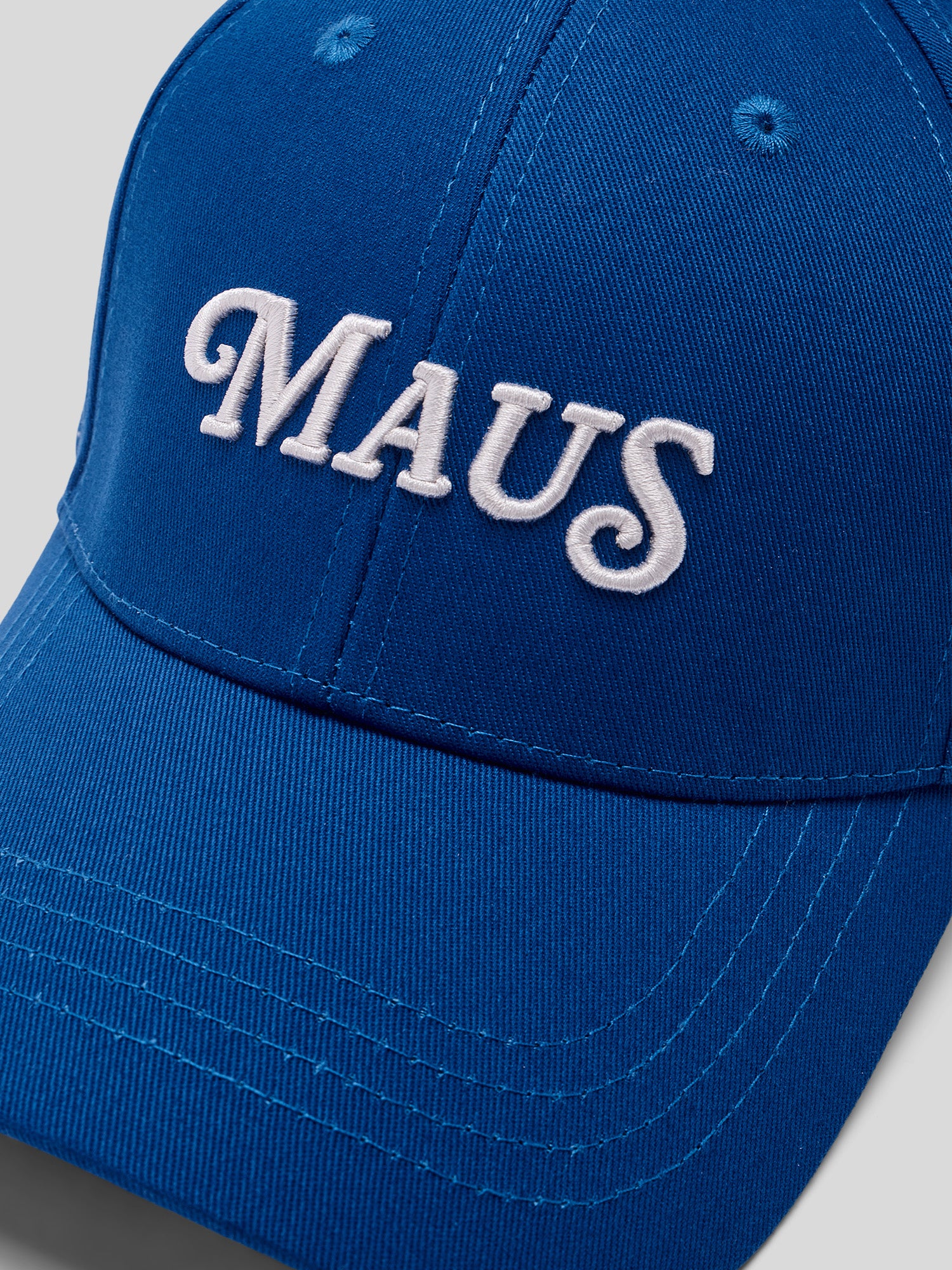 Nahaufnahme der blauen Baseballcap mit weiß gesticktem Schriftzug „MAUS“.