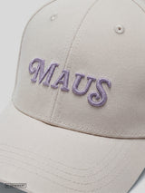Detailansicht einer Off-White Cap aus Baumwoll-Twill mit gebogenem Schirm. Zu sehen ist der gestickte „MAUS“-Schriftzug in Helllila auf der Vorderseite sowie die Struktur des Materials und der Stickerei.