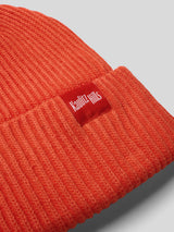 Nahaufnahme der orangefarbenen Strickmütze mit rotem Label „Kaulitz Hills“ am Bund.