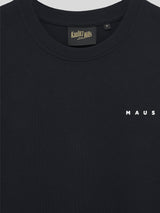 Nahaufnahme der Vorderseite des schwarzen T-Shirts mit kleinem weißen Schriftzug „MAUS“ auf Brusthöhe und Kaulitz Hills Label im Kragen.