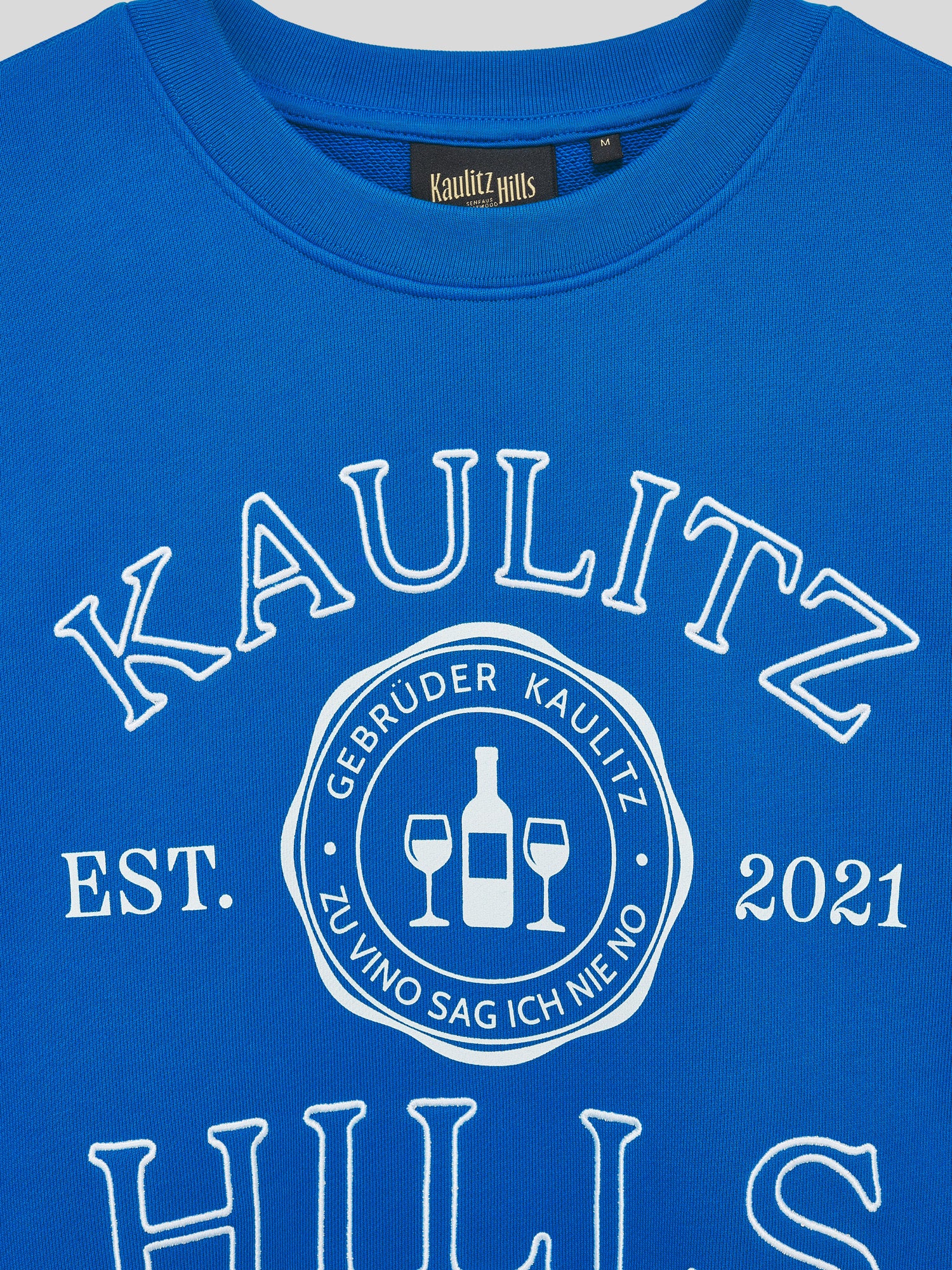 Nahaufnahme des Frontprints/Stick auf blauem Kaulitz Hills Sweatshirt mit Logo „Gebrüder Kaulitz – Zu Vino sag ich nie No“.