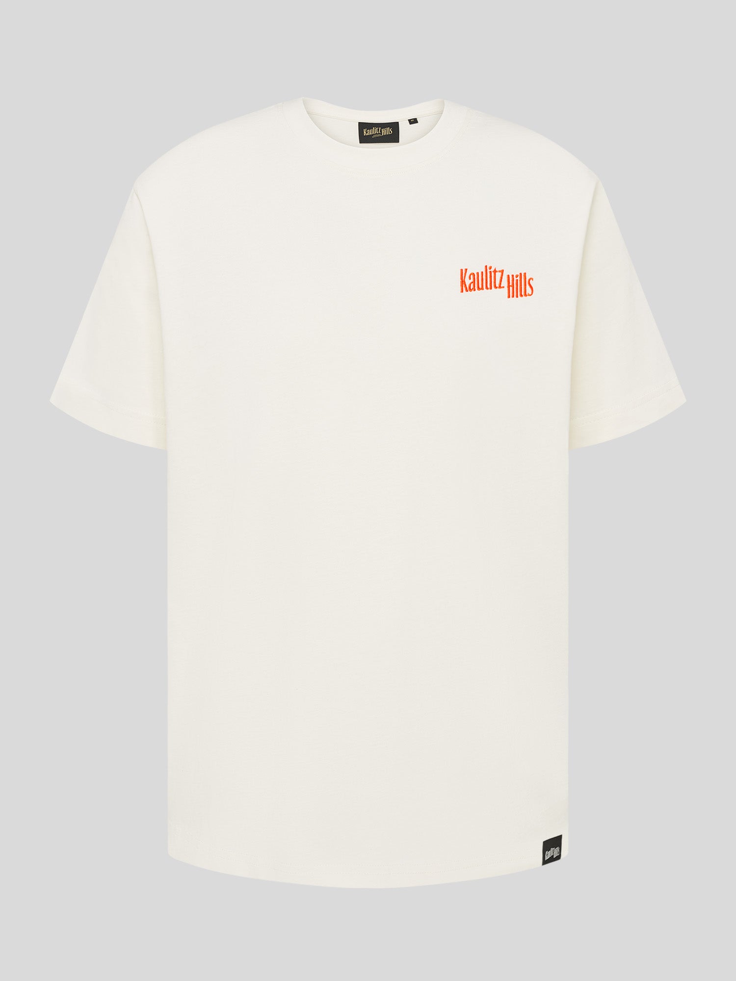 Weißes T-Shirt mit kleinem orangefarbenem Stickschriftzug „Kaulitz Hills“ auf der Brust.