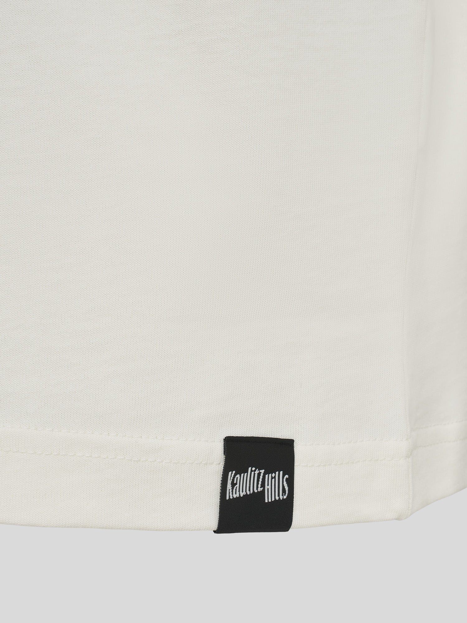 Nahaufnahme des schwarzen „Kaulitz Hills“-Labels am Bund des weißen T-Shirts.