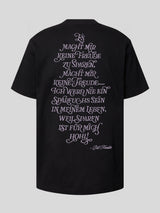 Rückansicht eines schwarzen oversized Kaulitz Hills T-Shirts mit großem lilafarbenem Statement-Print und Bill-Kaulitz-Signatur.